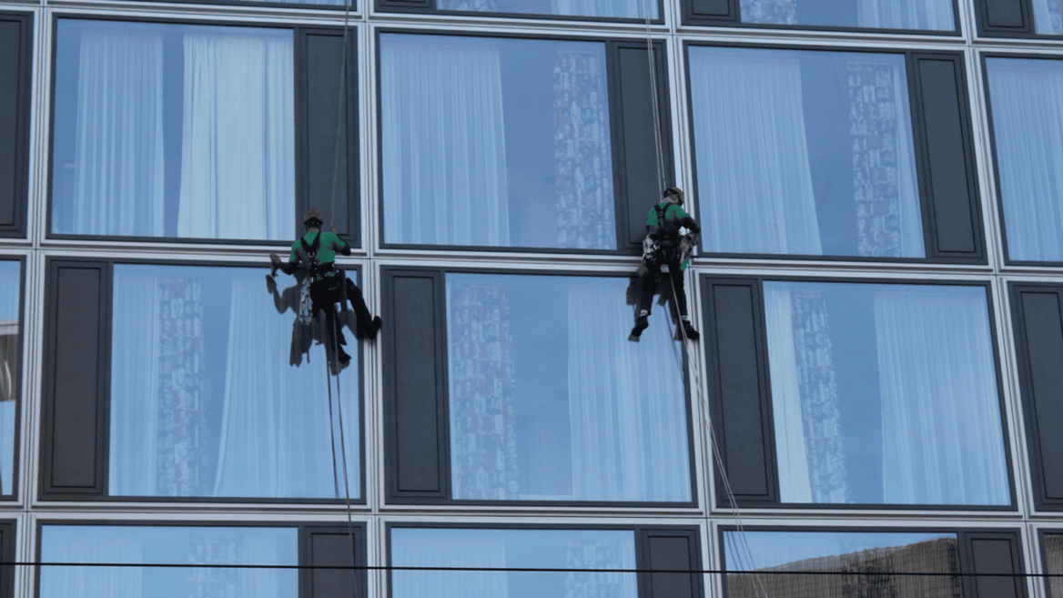dos personas limpiando al exterior ventanas de un edificio colgados