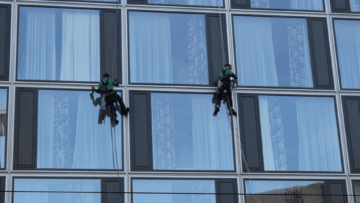 dos personas limpiando al exterior ventanas de un edificio colgados