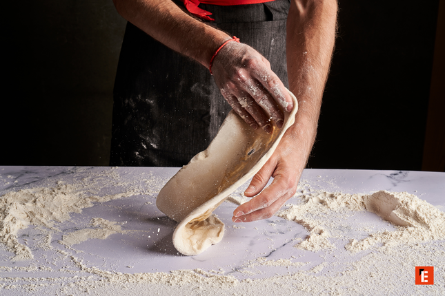 manos artesanas estirando masa de pizza