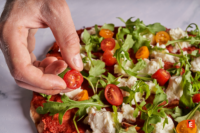 mano coloca tomate en pizza artesanal fresca