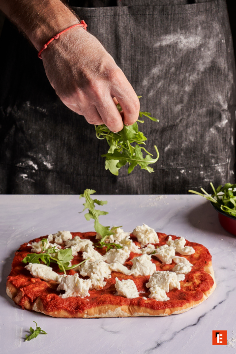 preparando pizza casera con rúcula y ricota