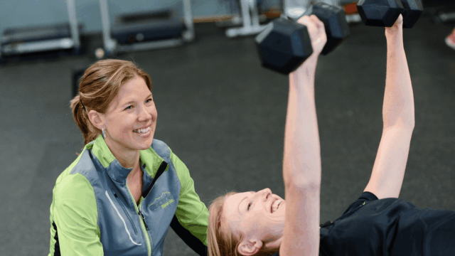 mujer haciendo pesas con entrenadora
