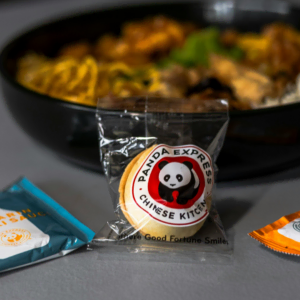 plate of panda express food with vegetables meat and rice, and a fortune cookie as well as sauces