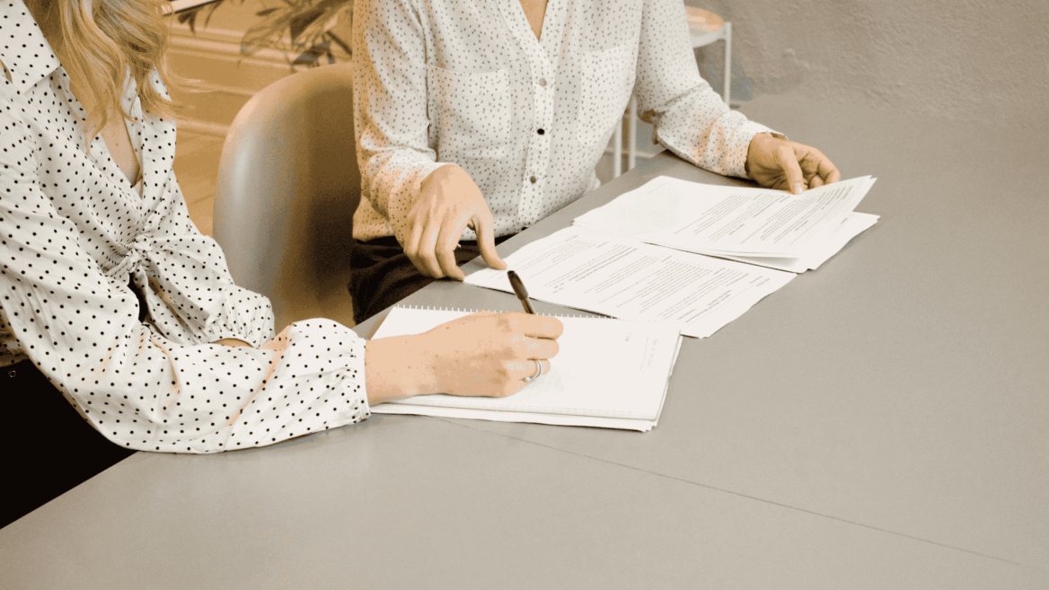 two women with shirts signing a document together, we do not see theur faces