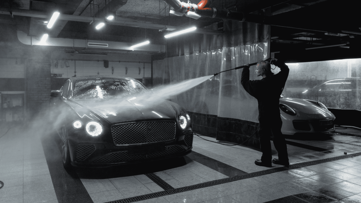 a woman in black sweater washing a black car using pressure washer hose