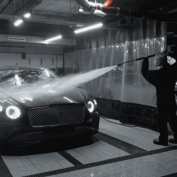 a woman in black sweater washing a black car using pressure washer hose