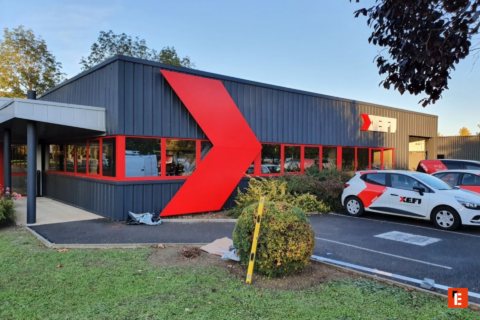 façade dentreprise grise avec flèche rouge et véhicules