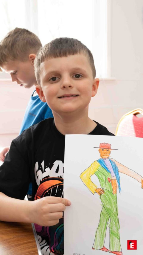 young boy proudly displays colorful drawing