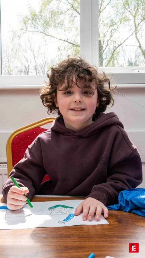 smiling curly haired child drawing at sunlit table