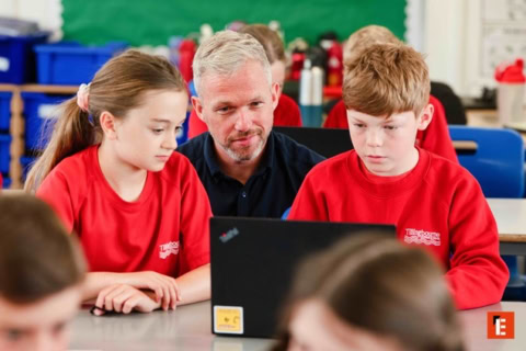 teacher guiding primary pupils on laptop activity