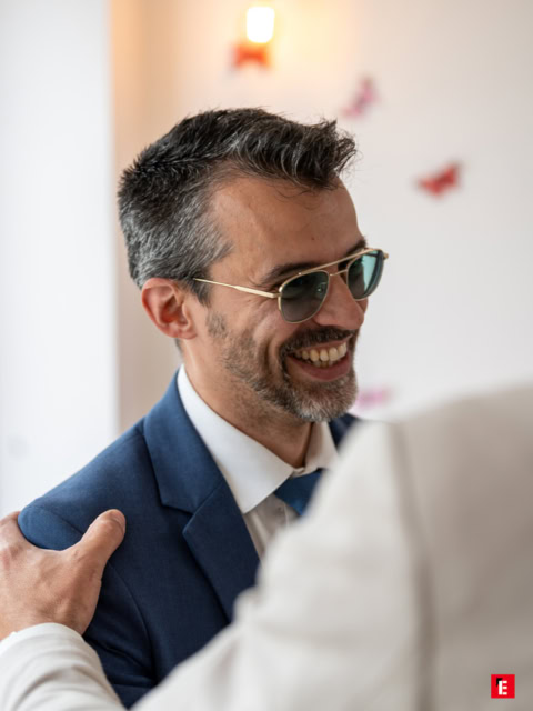 homme souriant en costume bleu et lunettes aviateur