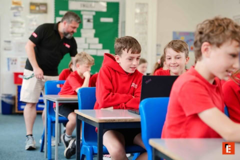 primary pupils sharing laptop in bright classroom