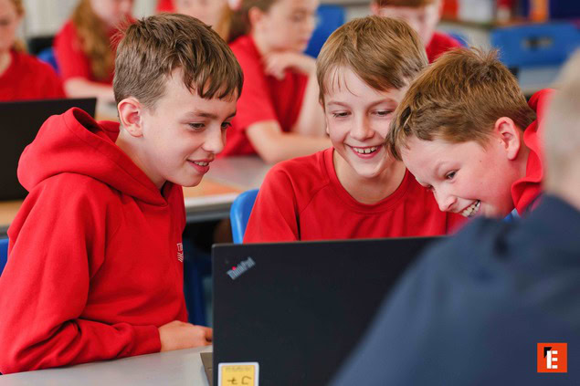 three schoolboys collaborating around a laptop in the classroom