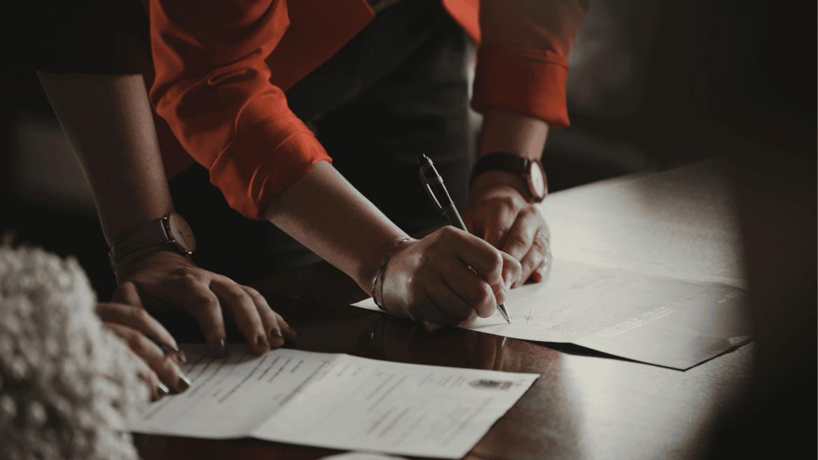 hands signing contract on wooden table