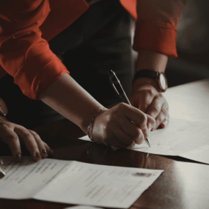 hands signing contract on wooden table