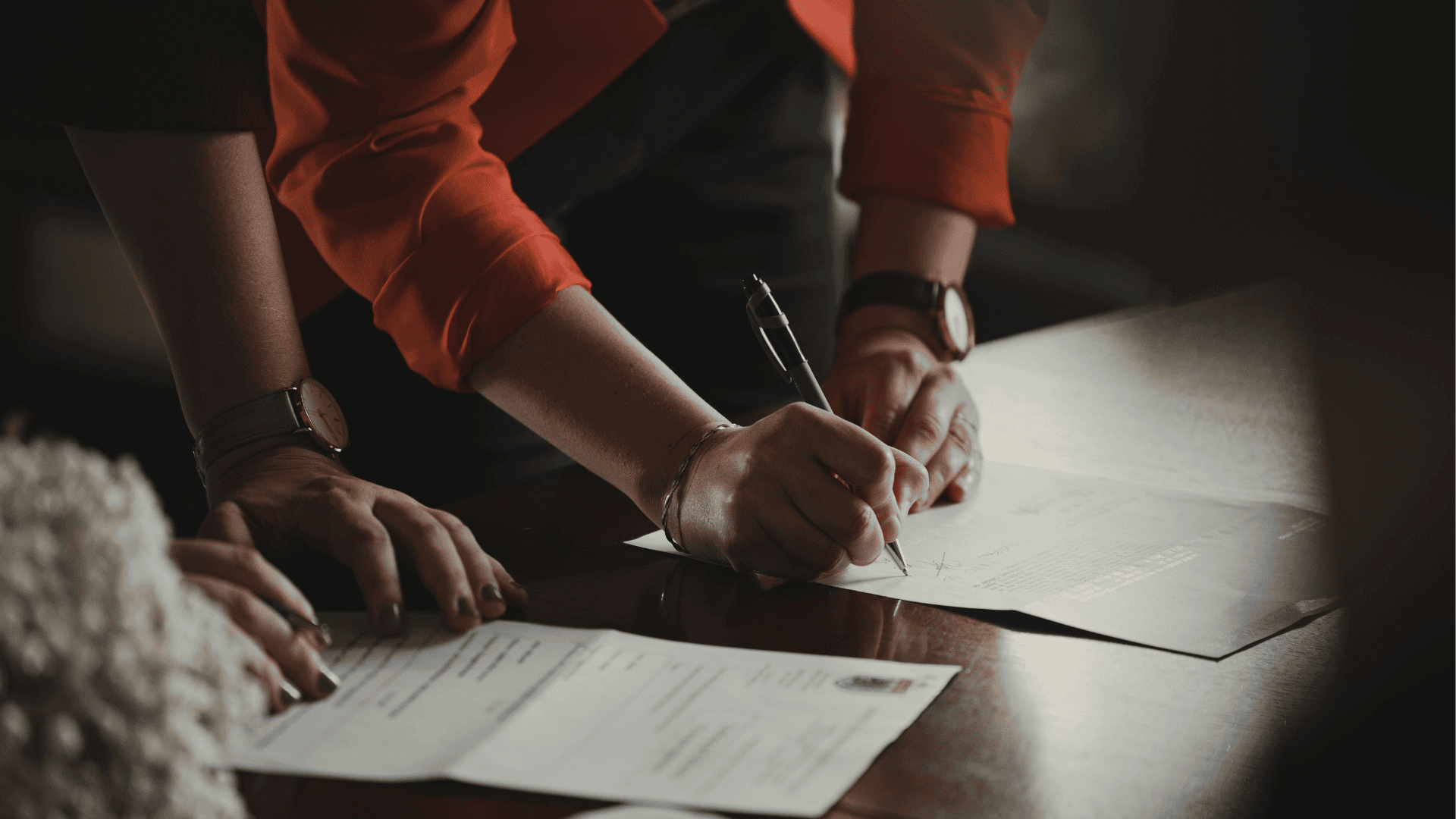 hands signing contract on wooden table
