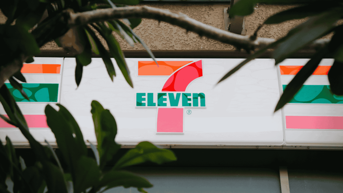 7 eleven sign framed by blurred green leaves