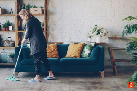 femme nettoyant le parquet devant canapé vert