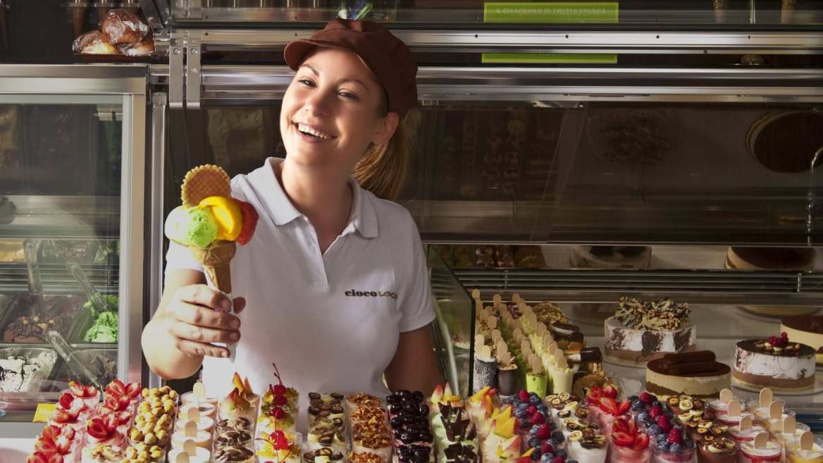 lächelnde verkäuferin reicht dreifarbige eistüte in eisdiele