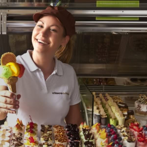 lächelnde verkäuferin reicht dreifarbige eistüte in eisdiele