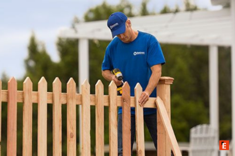 man installing wooden picket fence in backyard