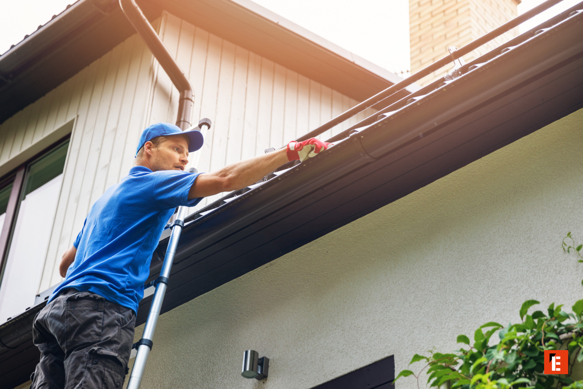 man on ladder cleaning roof gutter near chimney