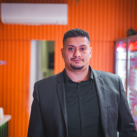 man in charcoal blazer headshot with orange backdrop