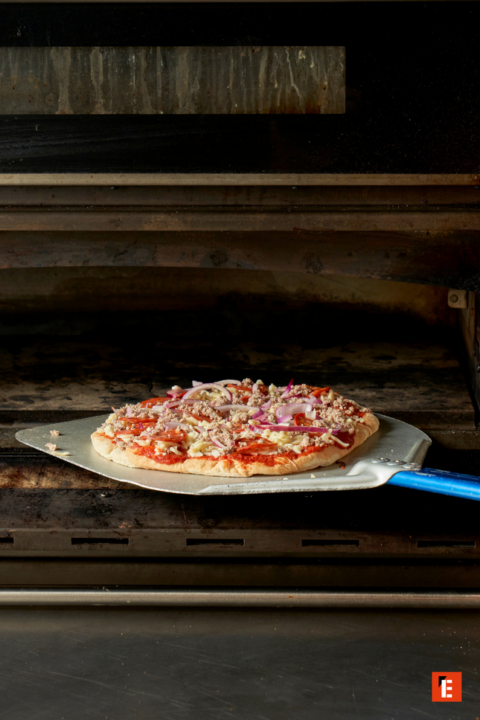 pizza cruda sobre paleta en horno industrial