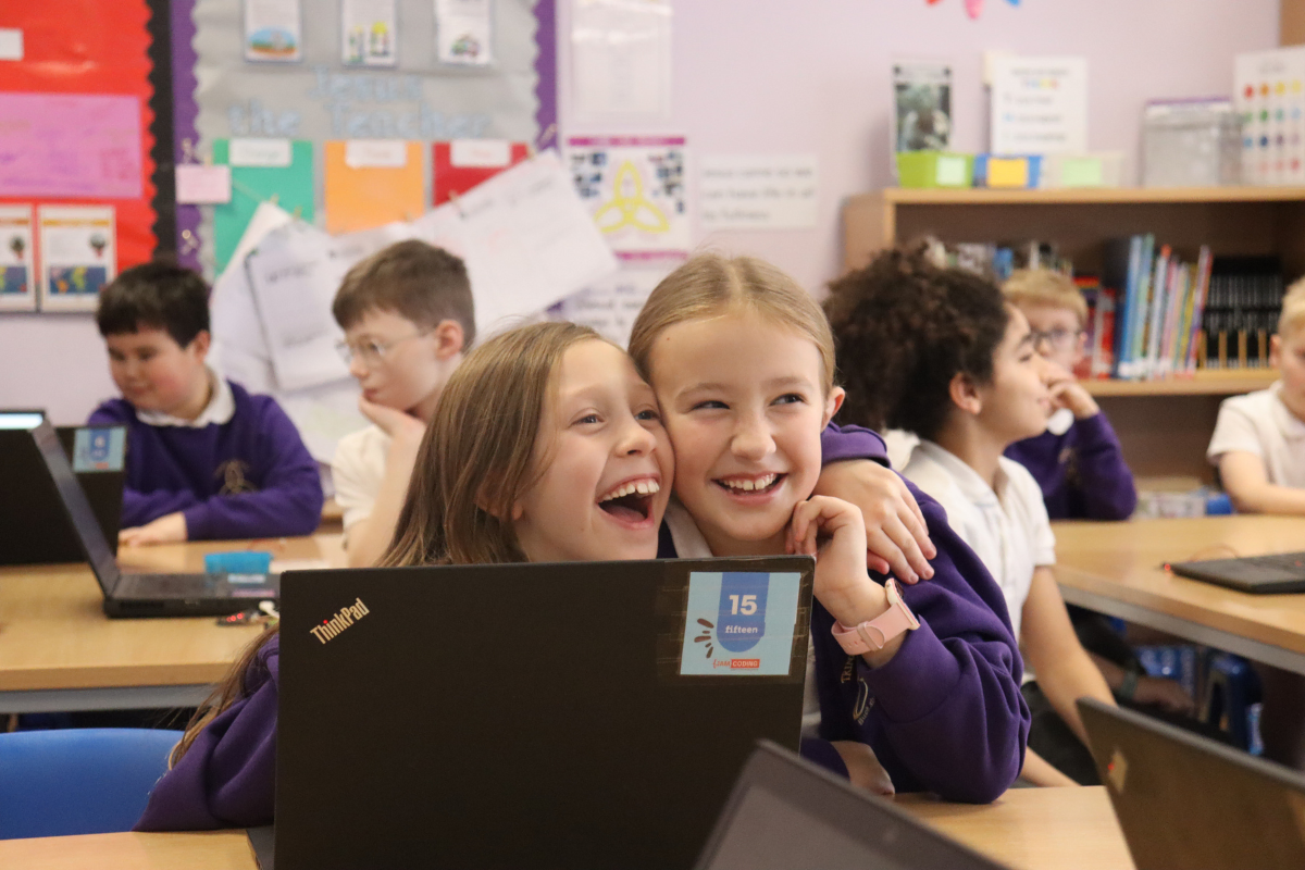 schoolchildren laughing and sharing a classroom laptop