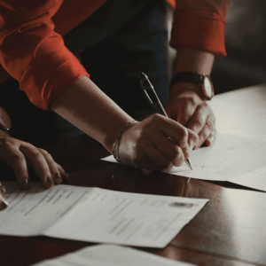 hands signing contract on wooden table