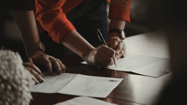 hands signing contract on wooden table