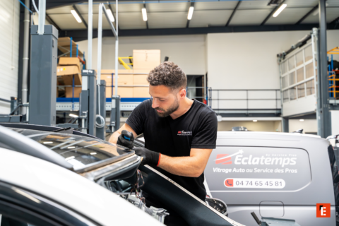 technicien vitrage auto réparant un pare brise en atelier