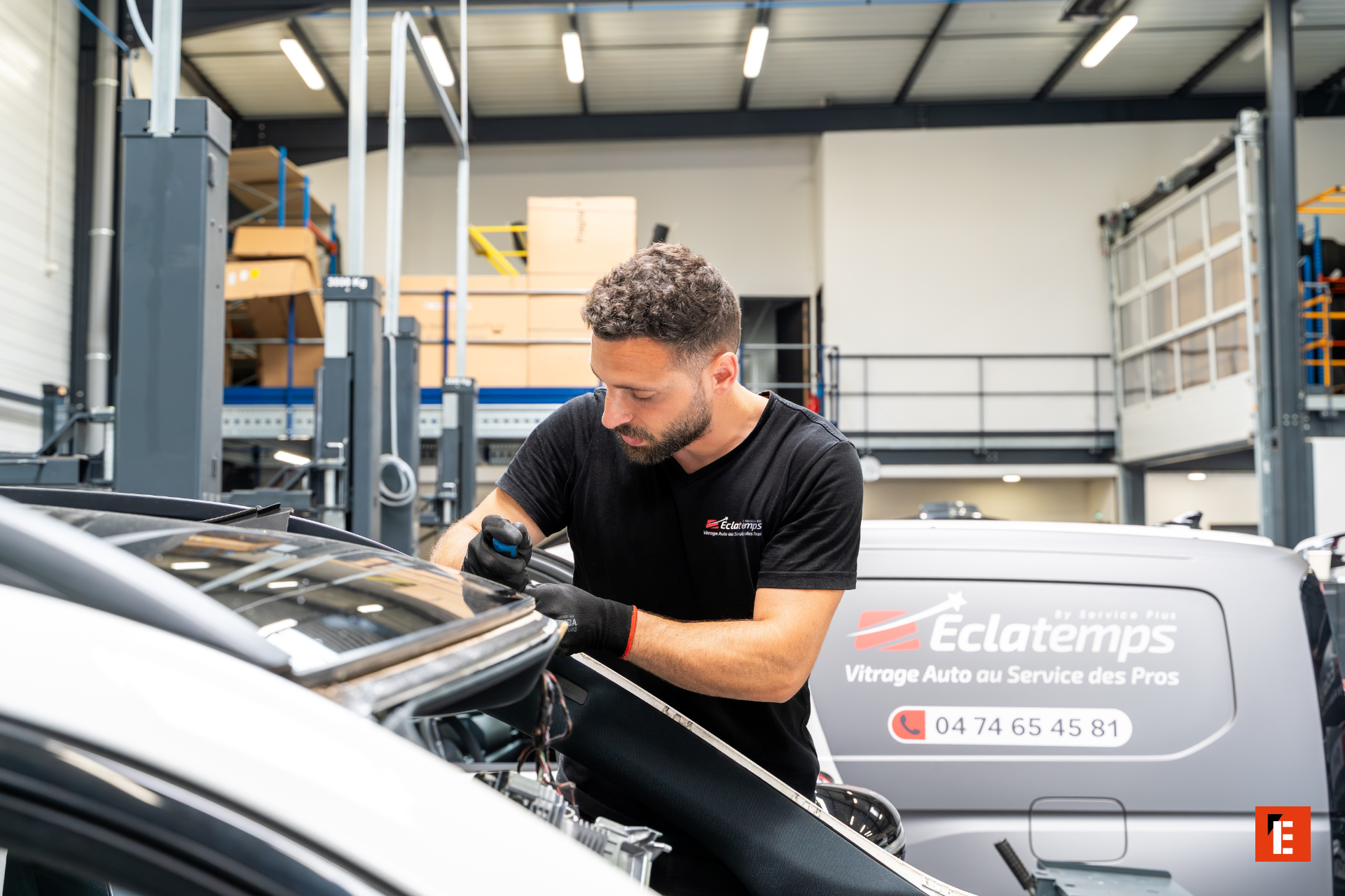 technicien vitrage auto réparant un pare brise en atelier