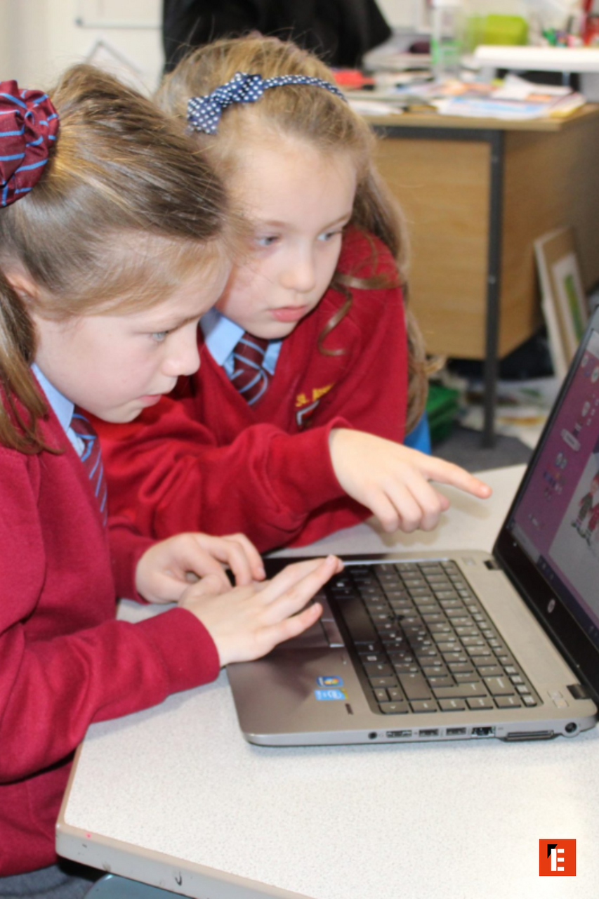two schoolgirls collaborating on a laptop in classroom