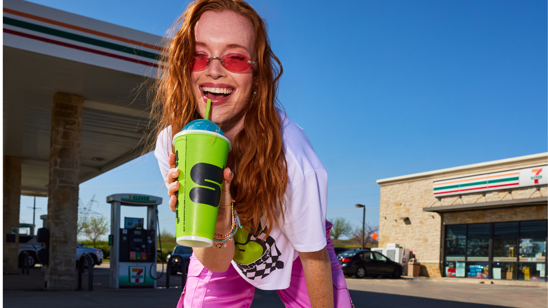 smiling woman holding 7‑eleven slurpee at gas station