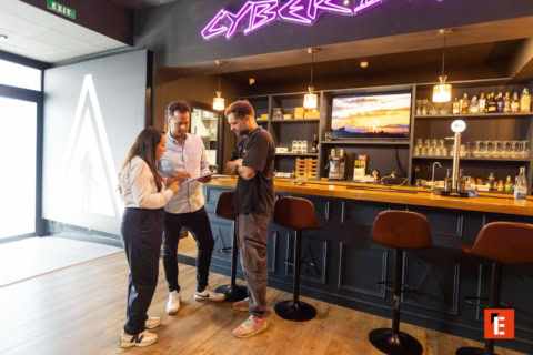 personal de bar revisando tablet junto a neón
