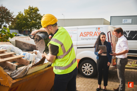 construction worker emptying skip beside aspray van