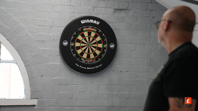 man studying winmau dartboard on grey wall