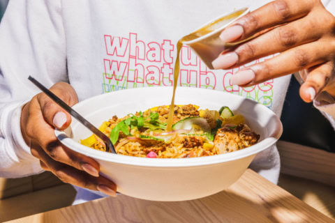 drizzling sauce over grilled chicken rice bowl