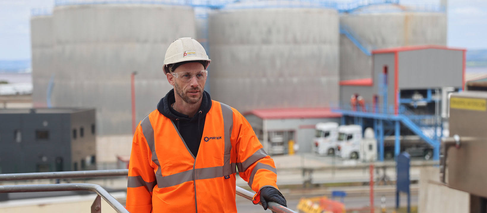 industrial worker in high visibility safety gear at tanks