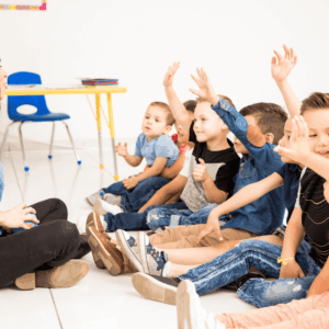 maestra y niños preescolares con manos levantadas