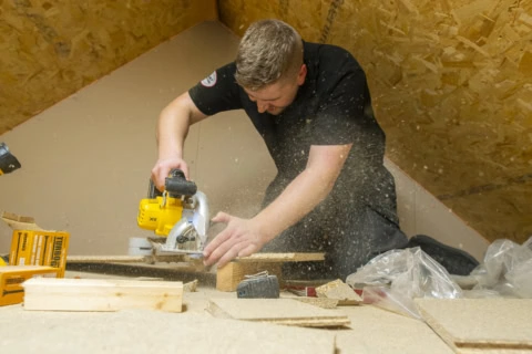 worker cutting wood with circular saw in attic