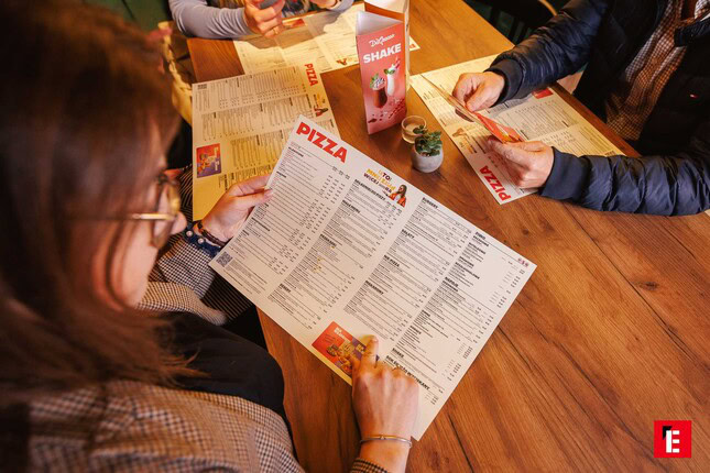 grupa zamawiająca pizzę przy drewnianym stole