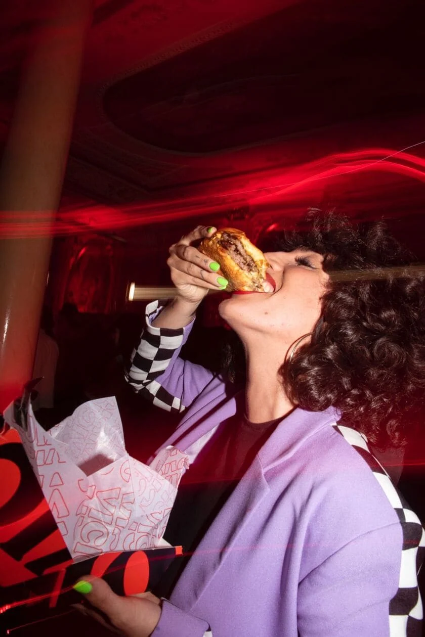 mujer comiendo hamburguesa callejera bajo neón