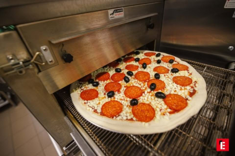 surowa pizza z pepperoni i oliwkami na taśmie pieca