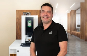 homme souriant en polo devant machine à café