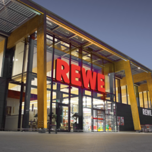 beleuchtete rewe glasfassade am abend mit holzstützen