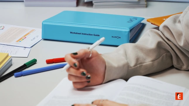 hand writing at study desk with kumon binder