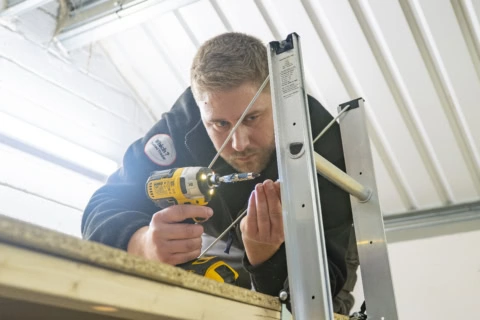 worker using cordless drill on metal frame