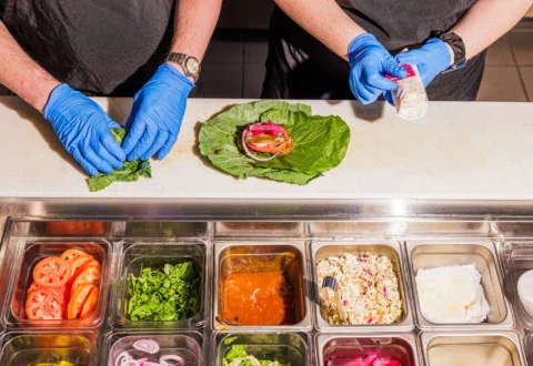 gloved hands assembling fresh lettuce wraps